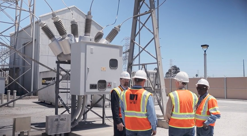 A group of workers standing in front of electrical equipment at a substation.