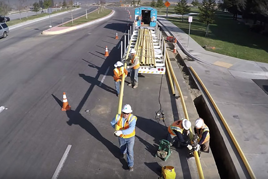 PG&E workers on a street pulling yellow gas pipes from the back of a truck