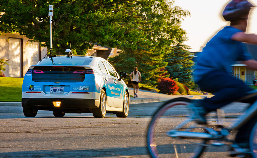 Electric car driving down a residential street among a bicylist and jogger