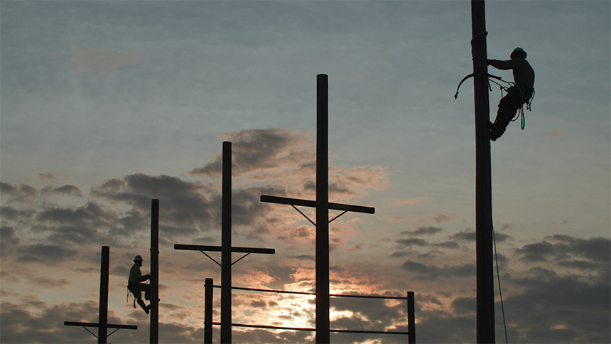 Silhouetted utility workers up on a pole at dawn